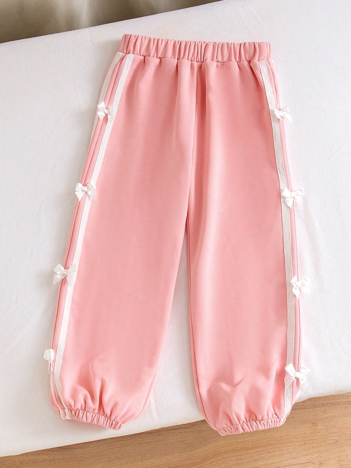 Little Girls' Pink Casual Pants, Decorated With White Side Tapes, Adding A Sporty Touch And A Retro Design Element. The Bow Design In The Middle Of The Tape Brings A Girlish And Playful Atmosphere. With Its Unique Side Design And Comfortable Wearing Exper